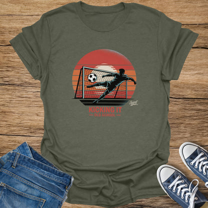 T-shirt graphic of soccer player kicking ball into net with sunset and text "Kicking It Old School".