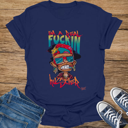 Dark blue t-shirt with cartoon graphic of a person and text "I'M A REAL FUCKIN HUSTLER".