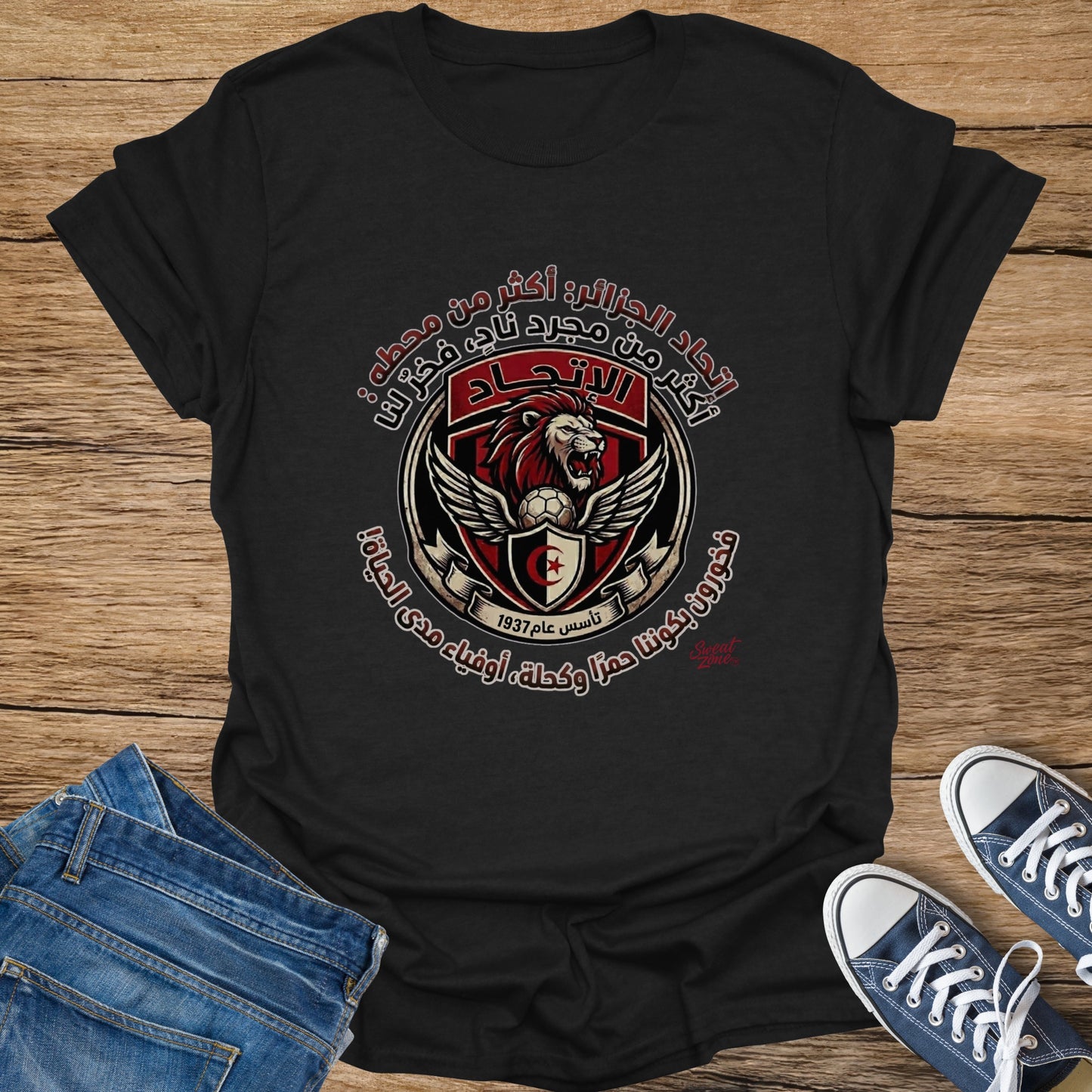 Black t-shirt with a shield logo featuring a lion, football, wings, and Arabic text.