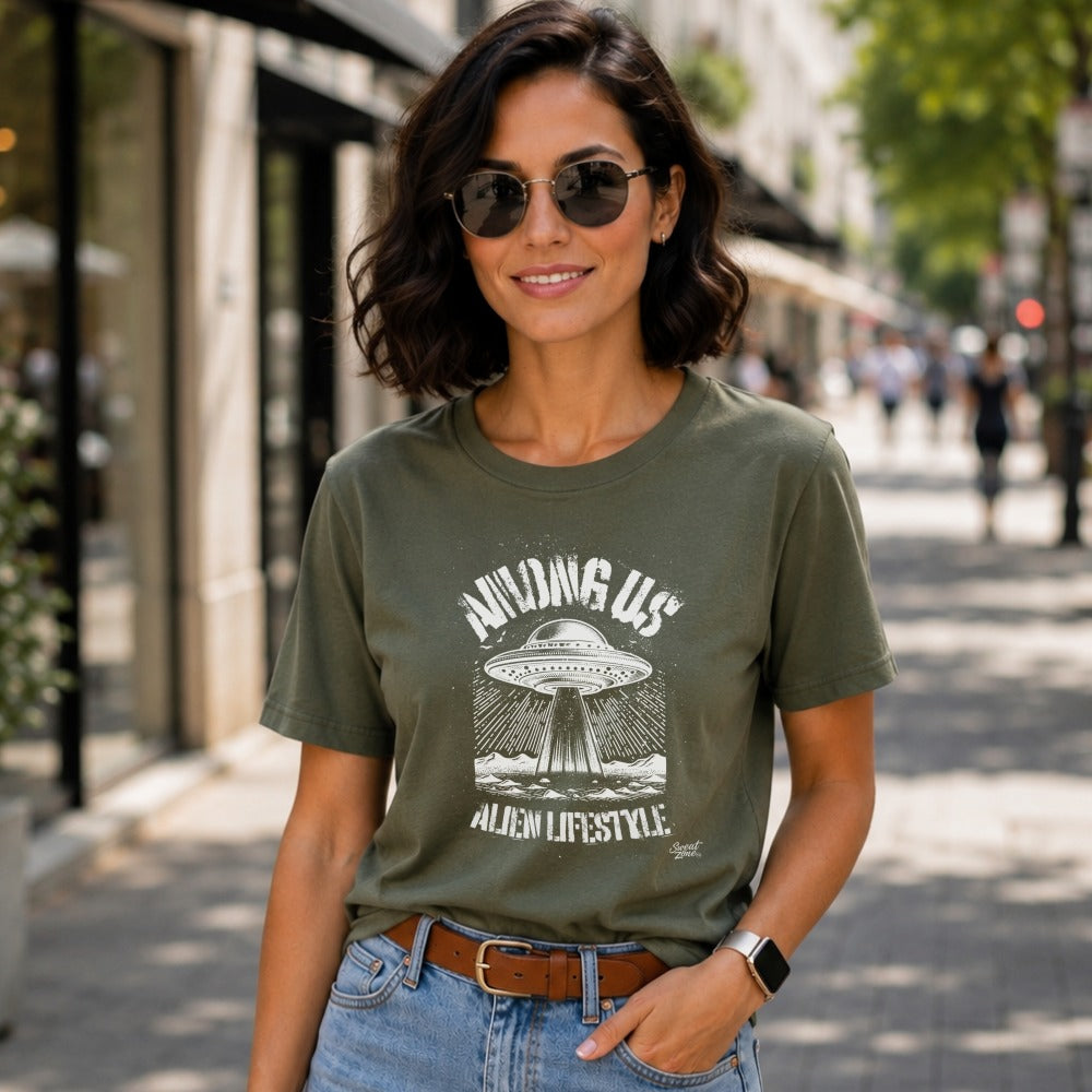 Woman wears olive t-shirt with "Among Us Alien Lifestyle" UFO graphic.