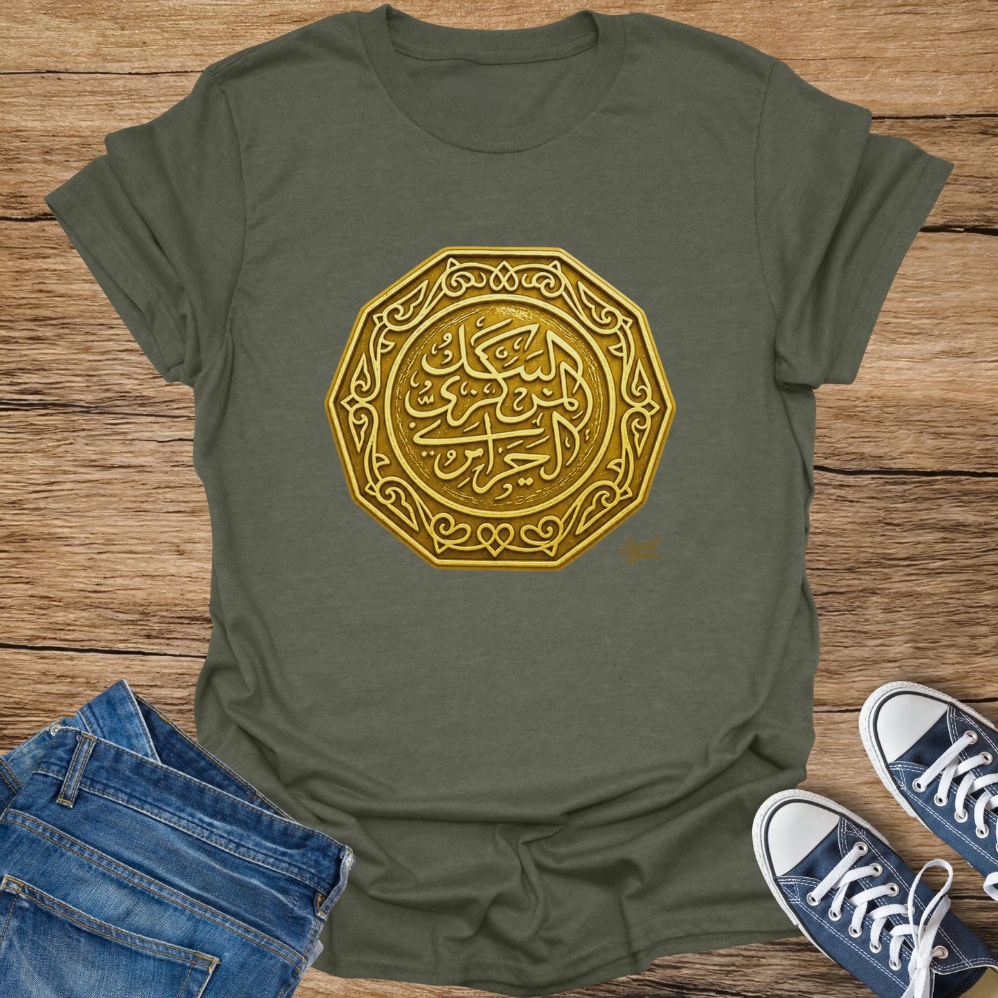 Olive t-shirt with ornate gold Arabic calligraphy on wooden background.