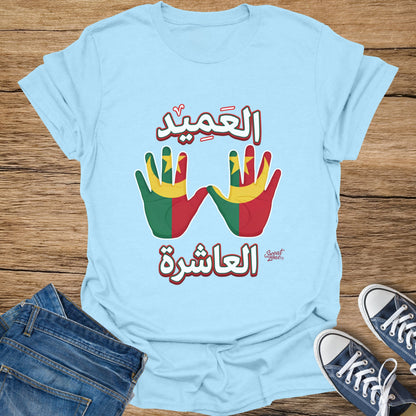Light blue t-shirt with Arabic text and hands painted with red, green, and yellow flags.