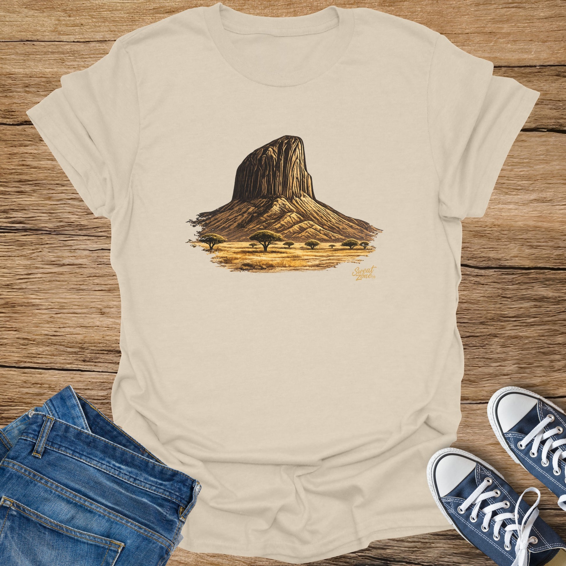Cream t-shirt with graphic of a large rock formation and savanna trees.