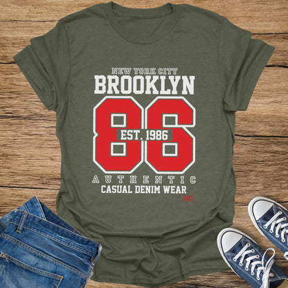 Olive green t-shirt with "Brooklyn Est. 1986" graphic and "Authentic Casual Denim Wear" text.