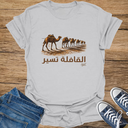 White t-shirt with a line of camels in the desert and Arabic text that reads "The caravan moves."