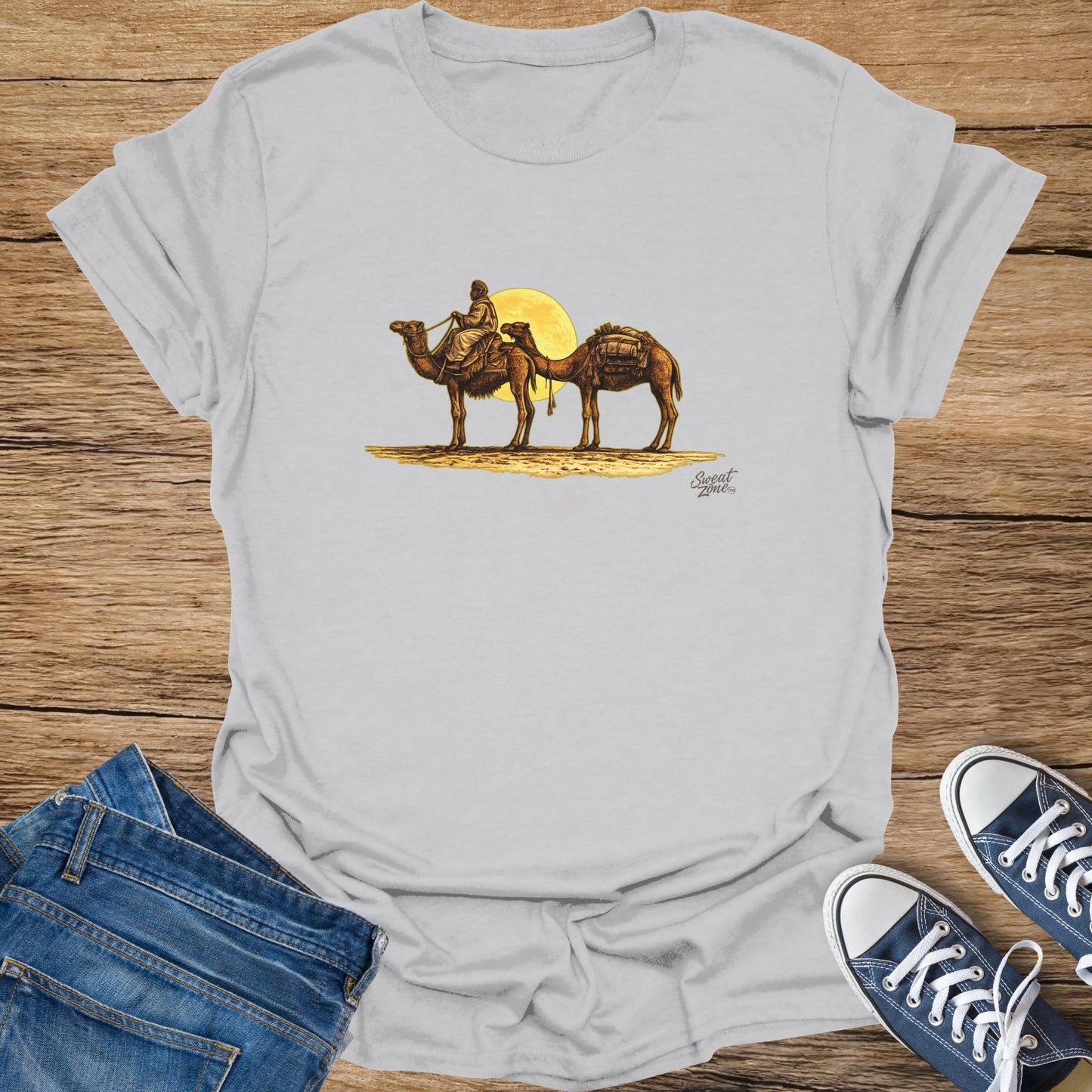 White t-shirt with graphic of a person riding a camel with another camel behind, against a yellow sun.