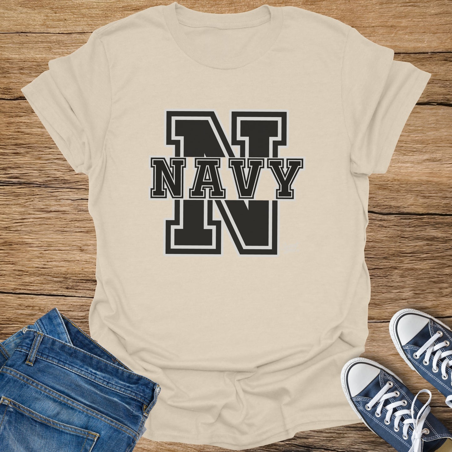Cream t-shirt with black "NAVY" text and "N" graphics, laid on wood with jeans and sneakers.