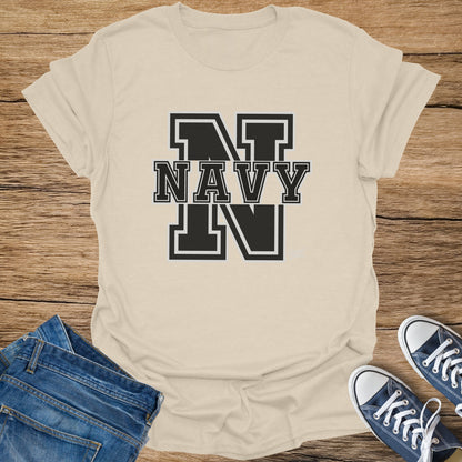 Cream t-shirt with black "NAVY" text and "N" graphics, laid on wood with jeans and sneakers.
