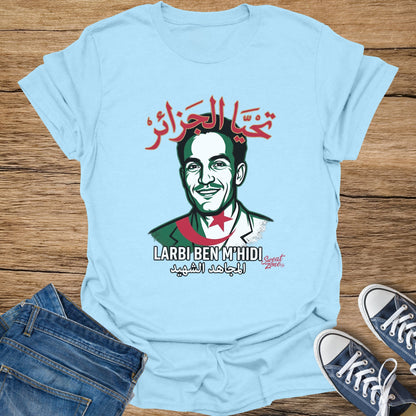 Light blue t-shirt with portrait of Larbi Ben M'hidi and Arabic text "تحيا الجزائر" and "المجاهد الشهيد".
