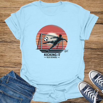 Light blue t-shirt with graphic of soccer player mid-kick with text "KICKING IT - OLD SCHOOL".