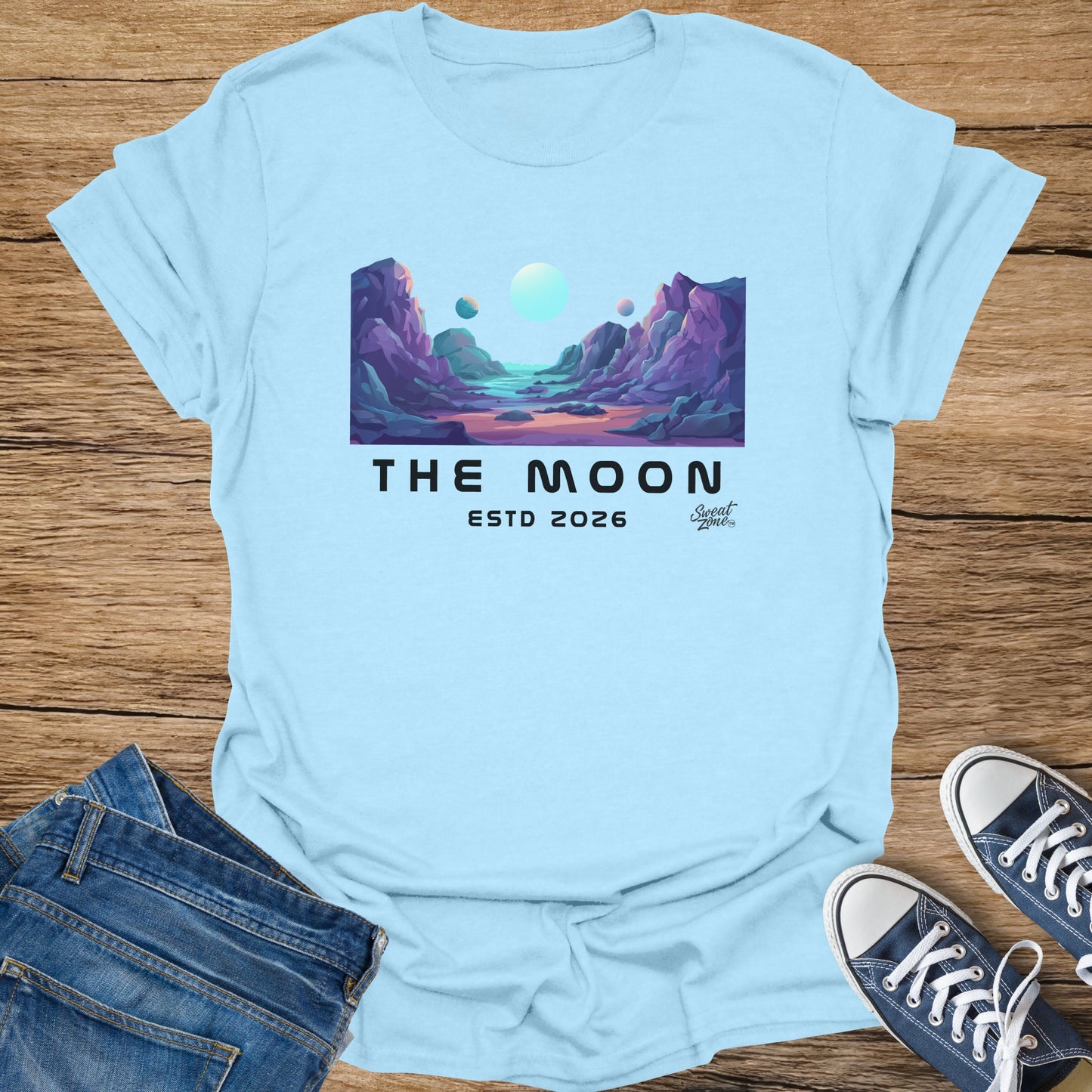 Light blue t-shirt with alien landscape graphic and text "The Moon ESTD 2026"