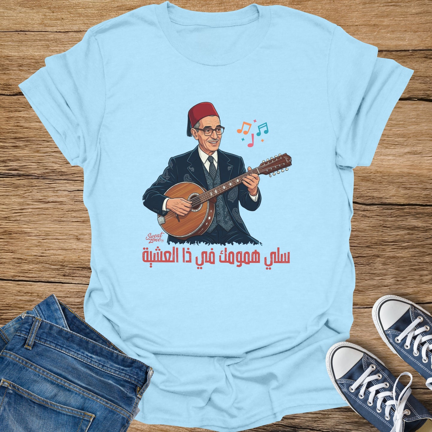 Light blue t-shirt with illustration of man playing oud, with Arabic text.