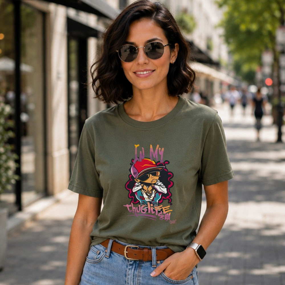 Woman wearing olive green t-shirt with "Lil My ThugLife" graphic and skull wearing a red hat.