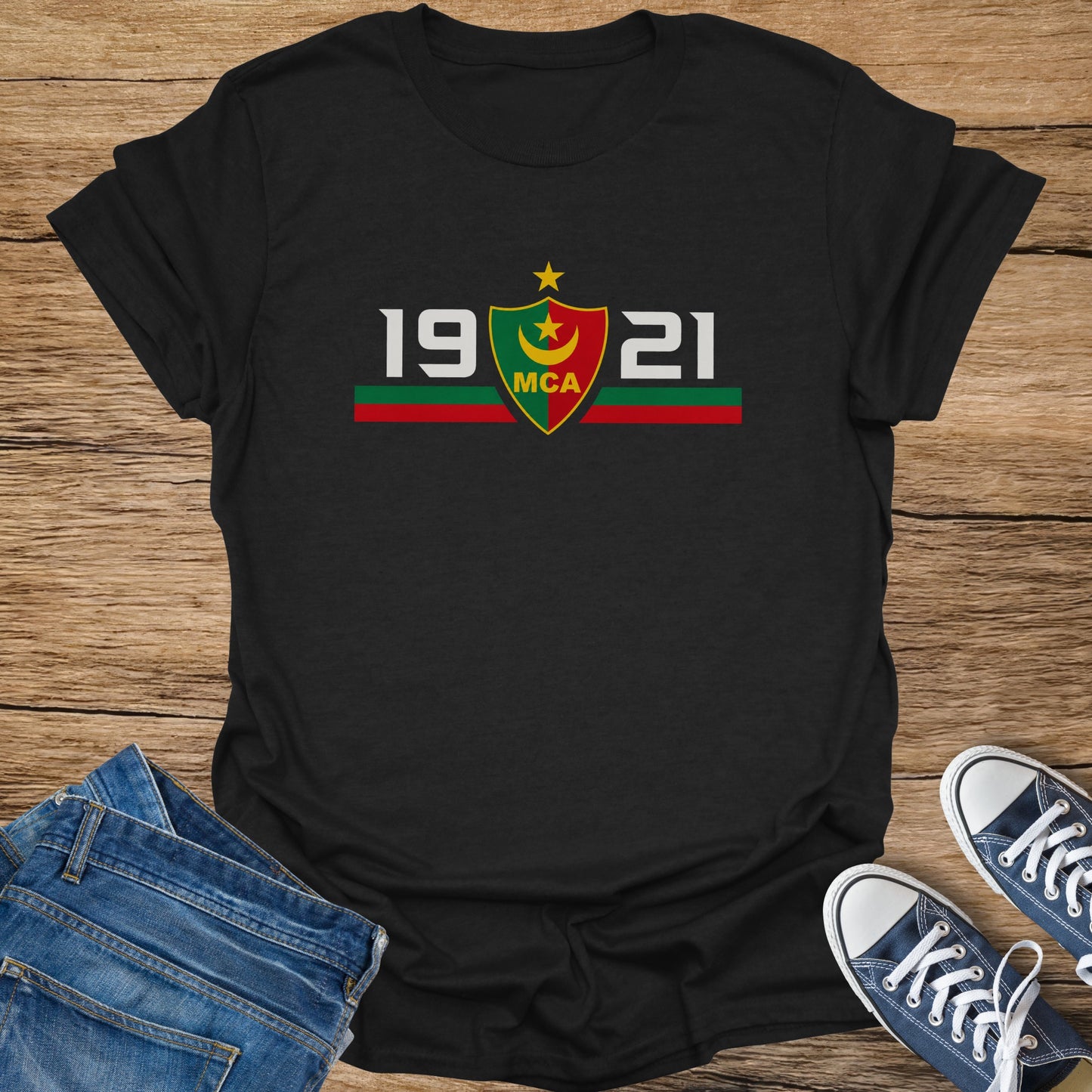 Black t-shirt with "19 MCA 21" and a crest, on a wooden surface.