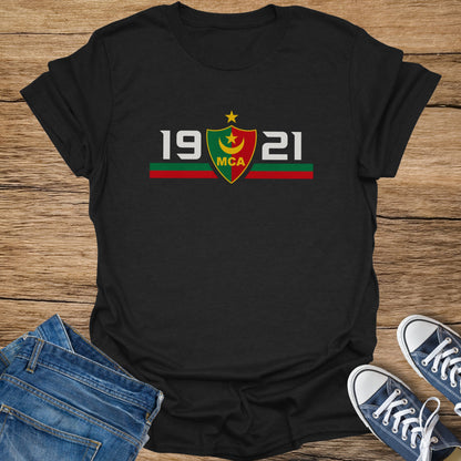 Black t-shirt with "19 MCA 21" and a crest, on a wooden surface.