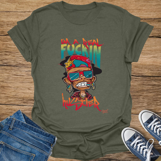 Olive green t-shirt with cartoon character and "I'm a real fuckin hustler" text.