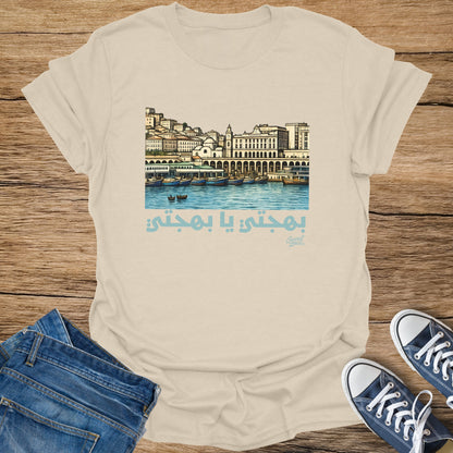 Beige t-shirt with illustration of a cityscape over water and Arabic text.