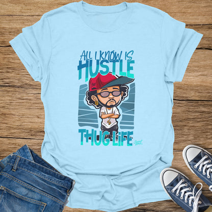Light blue t-shirt with cartoon character and text "All I Know Is Hustle Thug Life".
