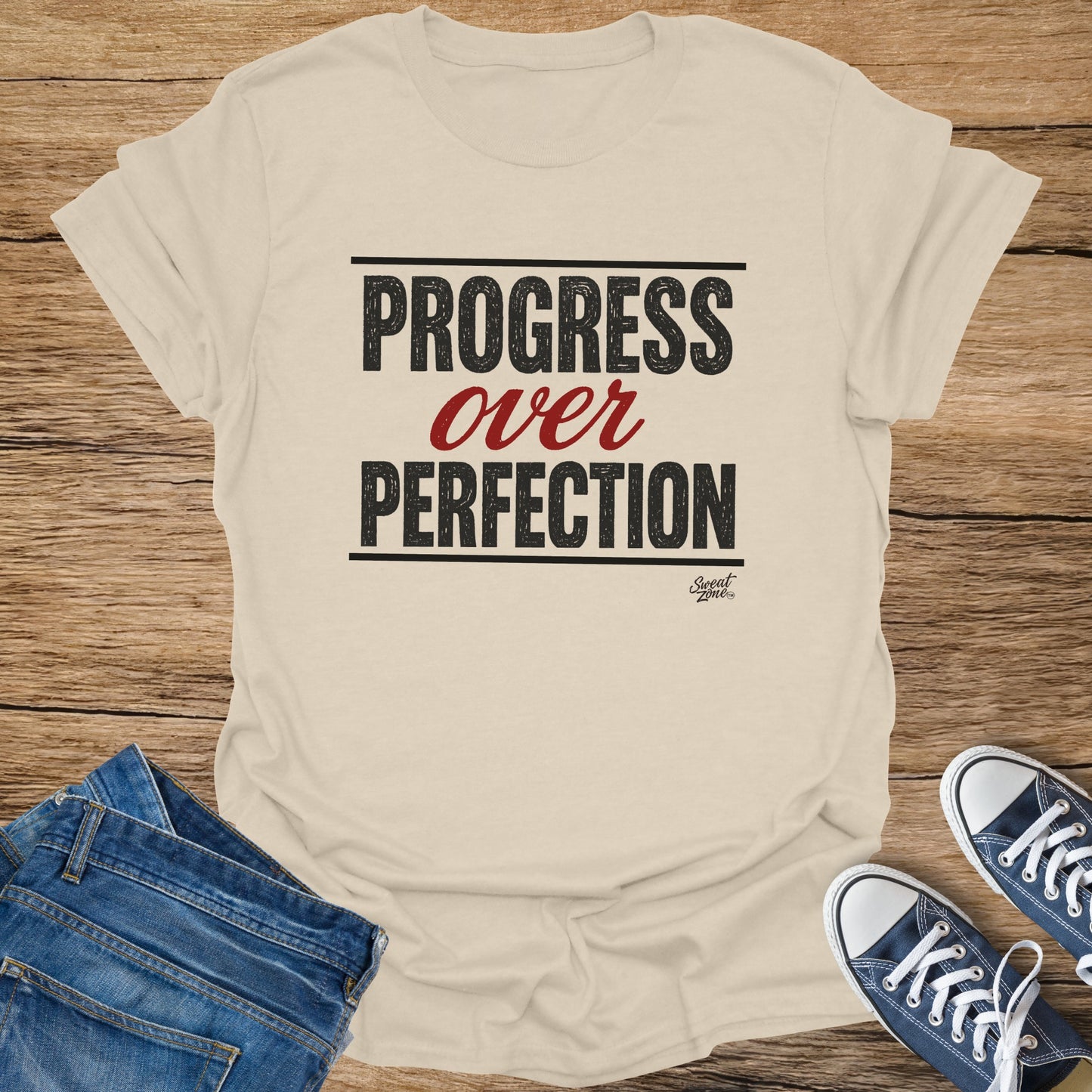 Beige t-shirt with black text "Progress over Perfection" and a small logo.