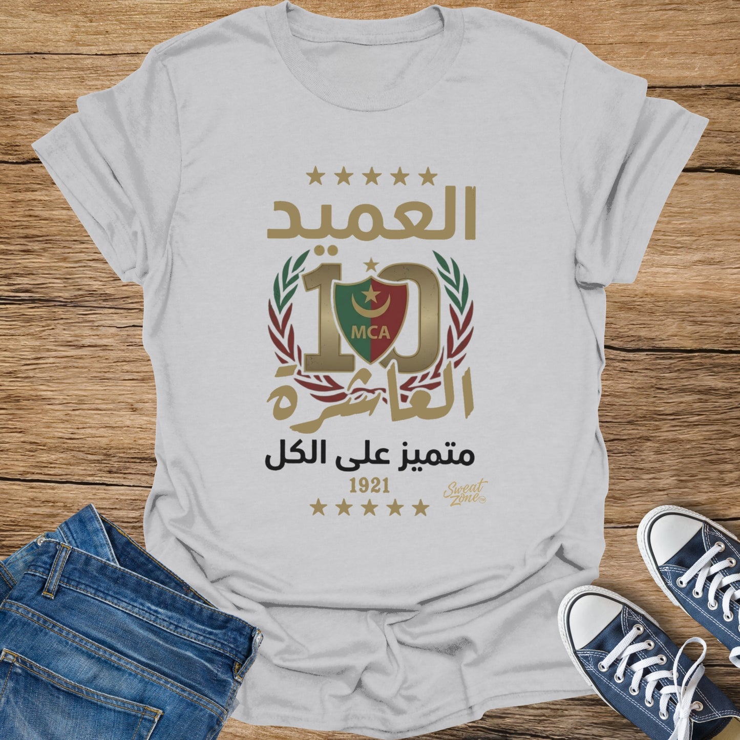 White t-shirt with gold Arabic text, "10" emblem, and "MCA" logo.