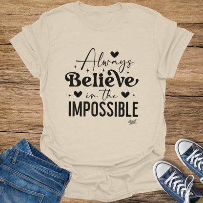 Light tan t-shirt with "Always Believe in the Impossible" text and small hearts.