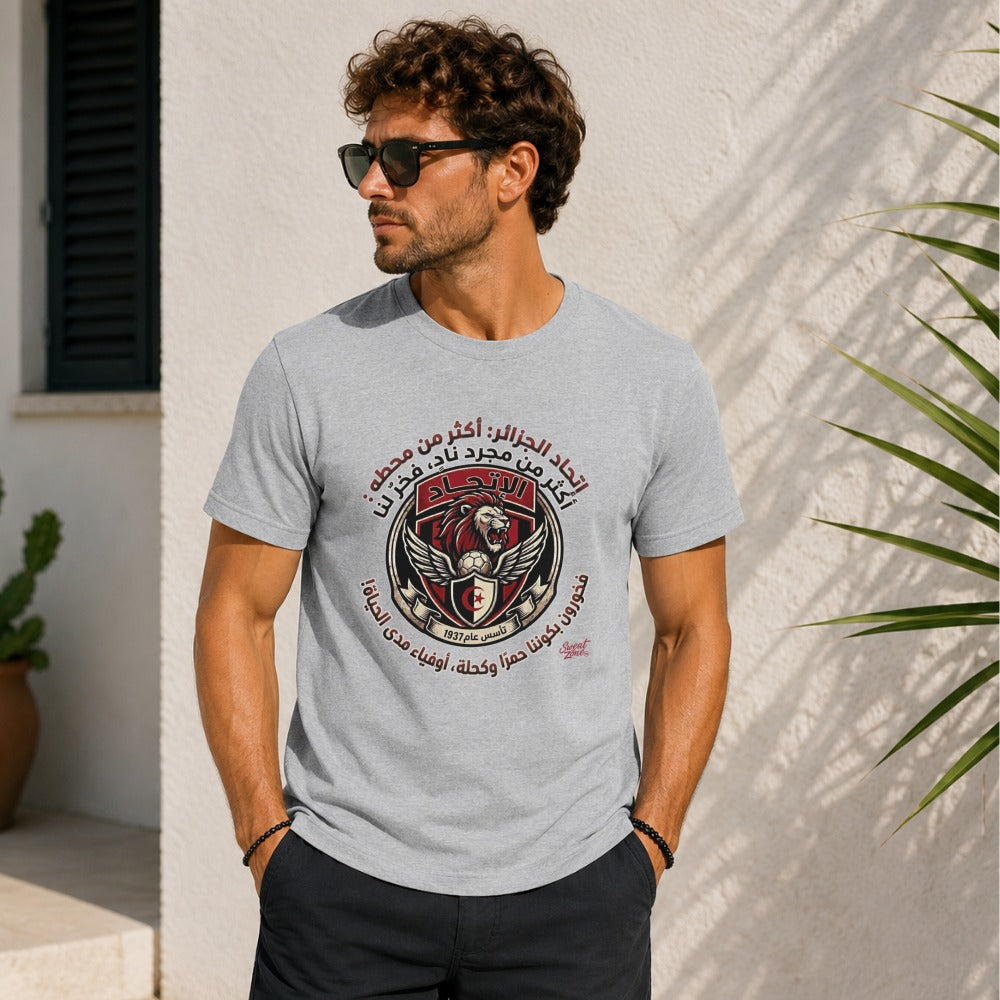 Grey t-shirt with circular emblem featuring a lion, soccer ball, and Arabic text.