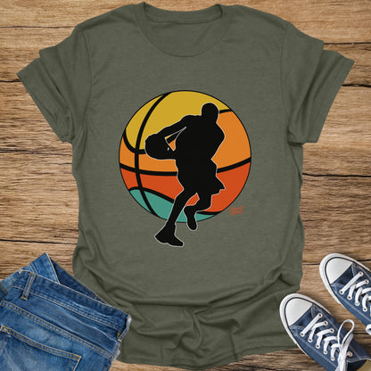 Olive green t-shirt with black graphic of basketball player and colorful sunset background.