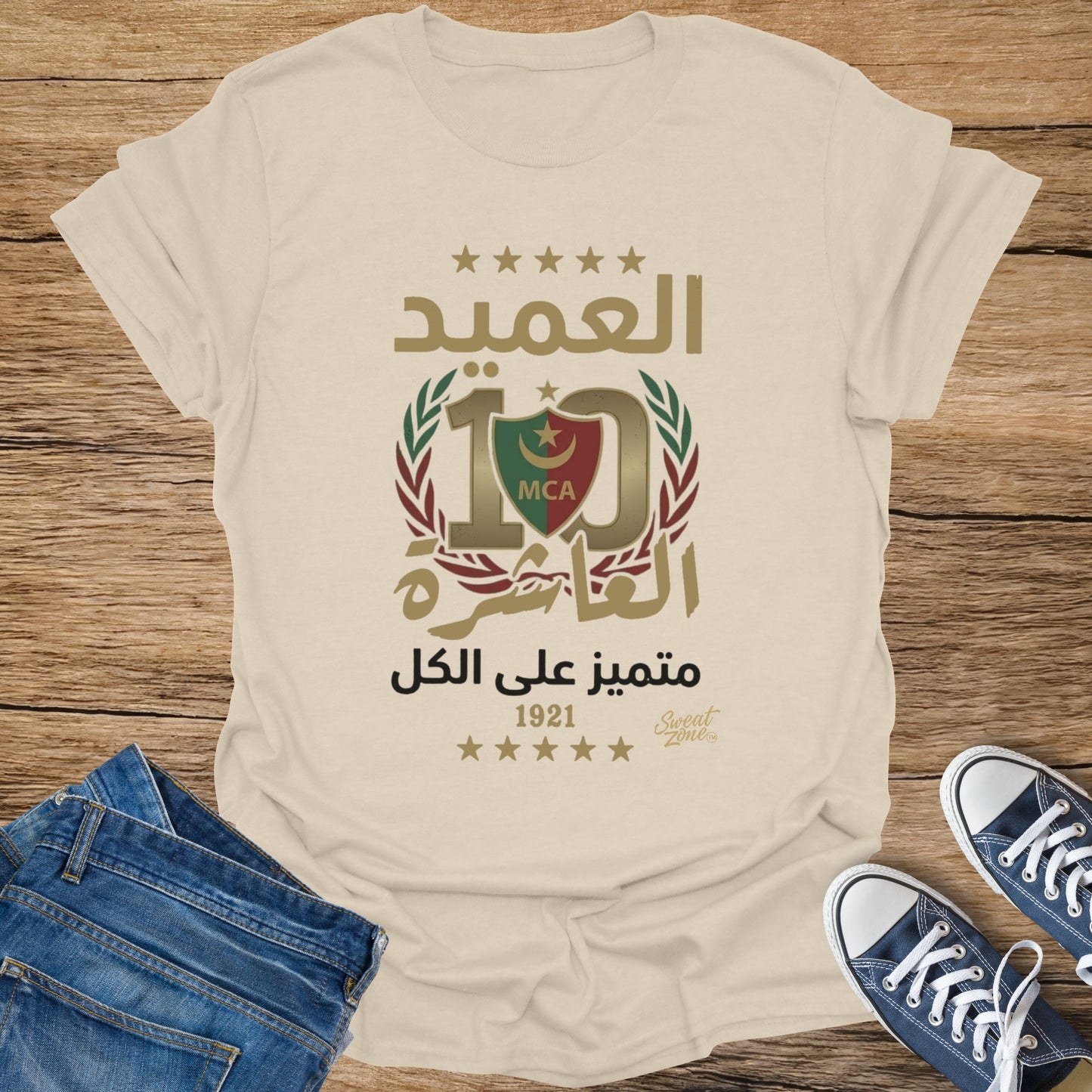 Cream t-shirt with Arabic text, a logo with 10, MCA, and "1921" date.