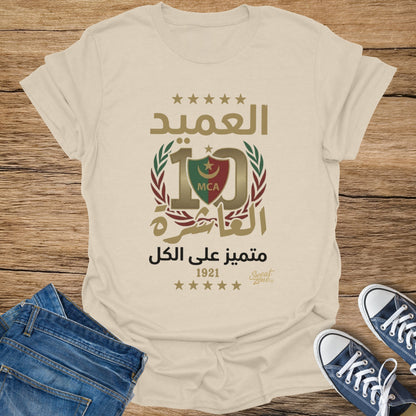 Cream t-shirt with Arabic text, a logo with 10, MCA, and "1921" date.