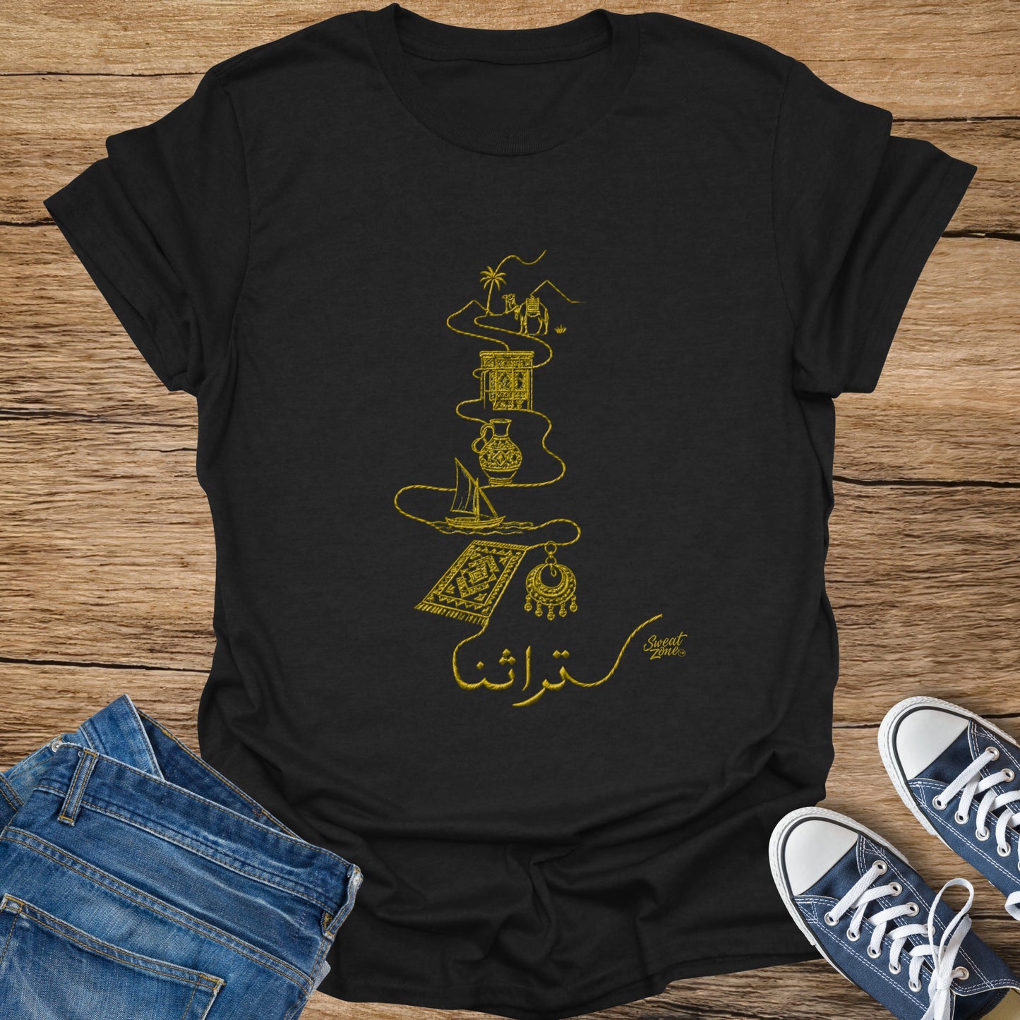 Black t-shirt with gold embroidered desert caravan, sailboat, rug, earring, and Arabic script.