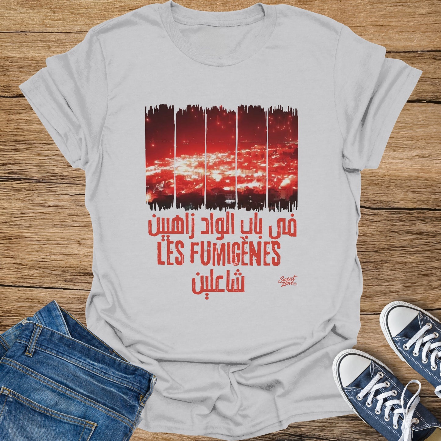 White t-shirt with red Arabic text and "LES FUMIGÈNES" above a city at night.
