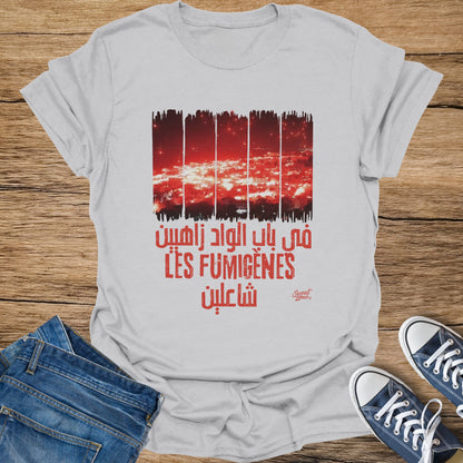 White t-shirt with red Arabic text and "LES FUMIGÈNES" above a city at night.