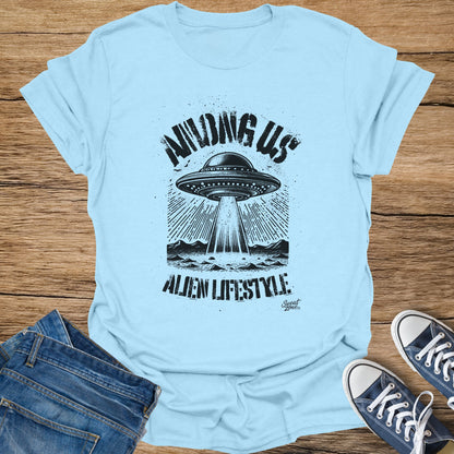 Light blue t-shirt with black graphic of UFO abducting a landscape, "AMONG US ALIEN LIFESTYLE" text.