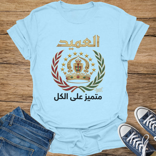 Light blue t-shirt with Arabic text and a crest with stars and a crown.