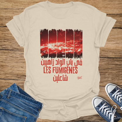 Cream t-shirt with red graphic depicting fireworks over a city and Arabic text.