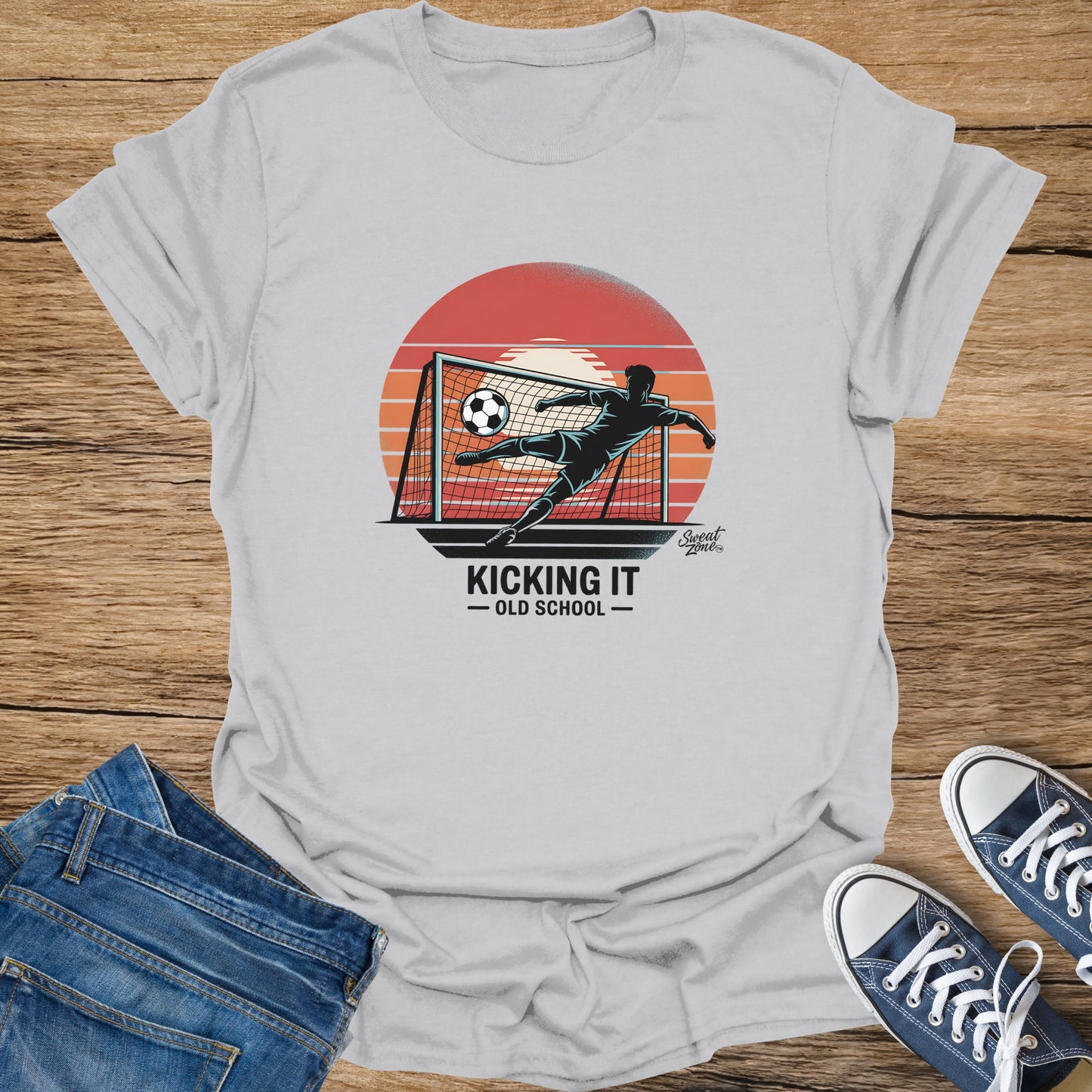 T-shirt graphic of soccer player kicking ball into a net with sunset and text "Kicking It Old School."