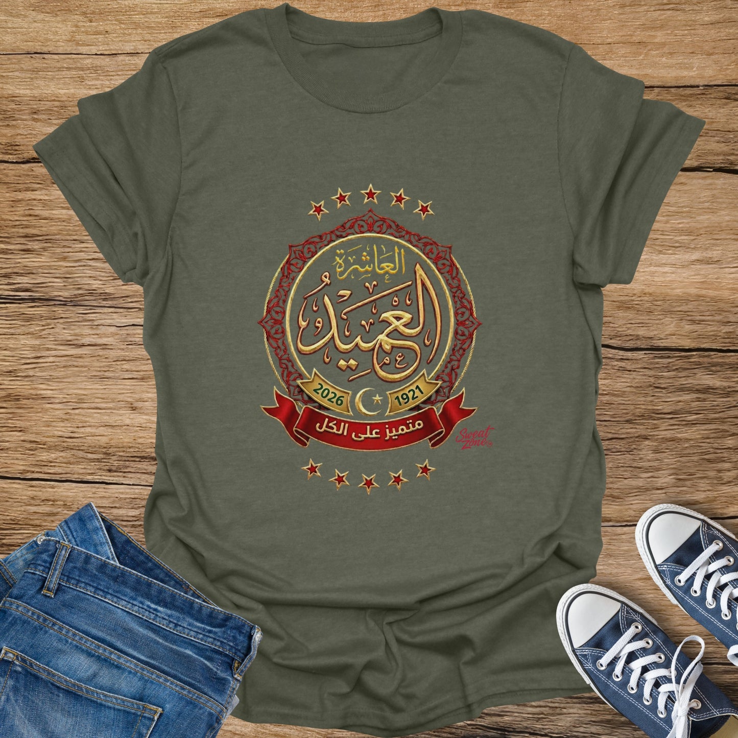 Olive green t-shirt with Arabic text, stars, and dates 2026 and 1921.
