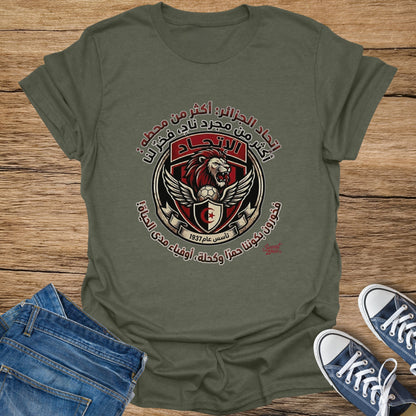 Green t-shirt with a circular crest featuring a lion, soccer ball, wings, and Arabic text.